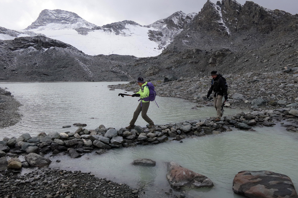 hikers with trekking poles crossing a glacier stream in the Grand Desert on the Haute Route Swiss Alps